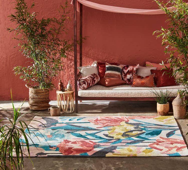 Colourful Verdaccio Rug Coral with decorative cushions and plants.
