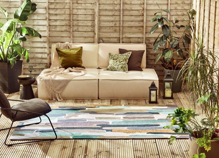 Cozy outdoor seating area with sea glass coloured rug and lush plants.