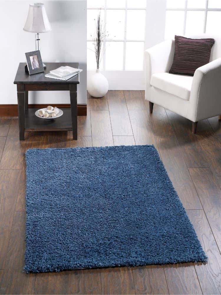 Dark teal plush rug in modern living room with white armchair and wooden floor.