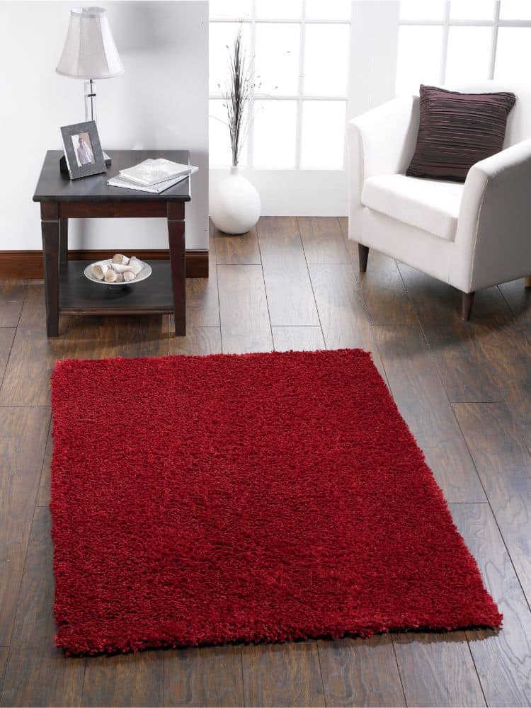 Red shaggy rug in modern living room with white armchair and side table.