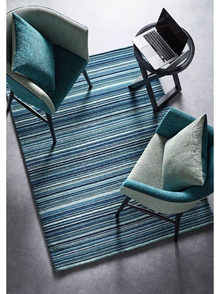 Blue and beige striped rug with two modern chairs and a laptop on a small table.