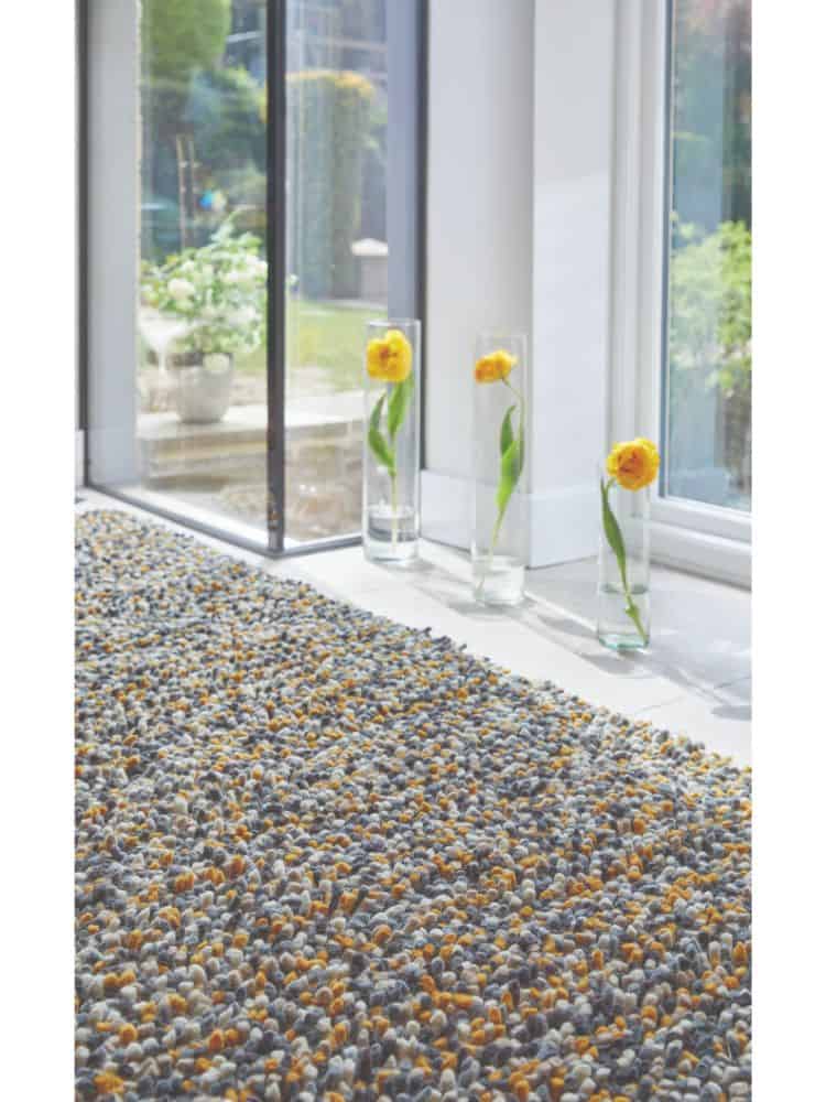 Close-up of a textured ochre shaggy rug on a bright sunlit floor.