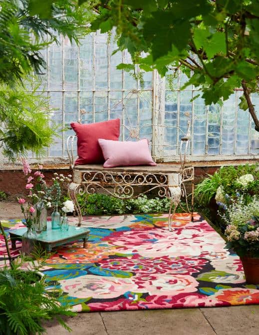 Vibrant floral rug in a greenhouse with cushions and plants.