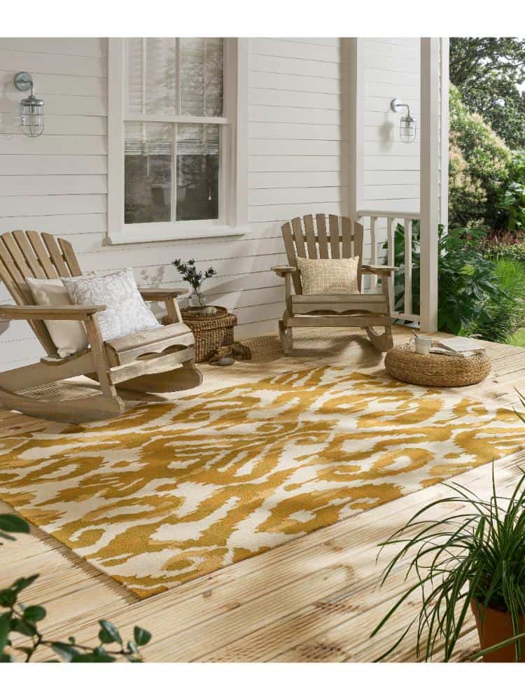 Outdoor porch with Kasuri Ochre rug, wooden chairs, and greenery.