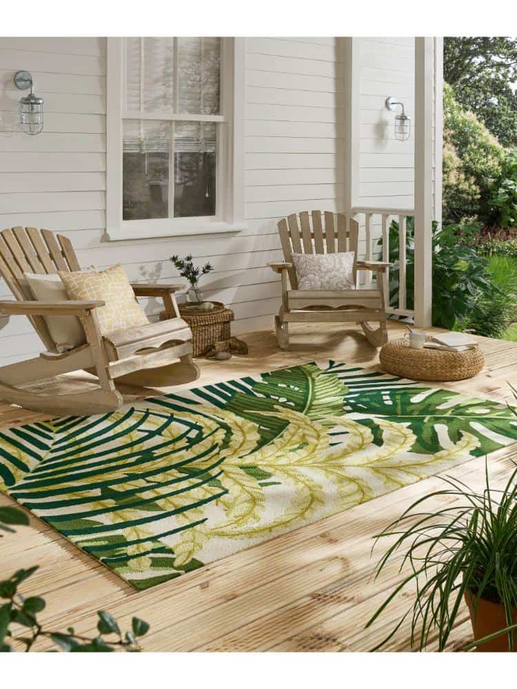 Outdoor patio with Manila Artichoke rug, wooden chairs, and lush greenery.