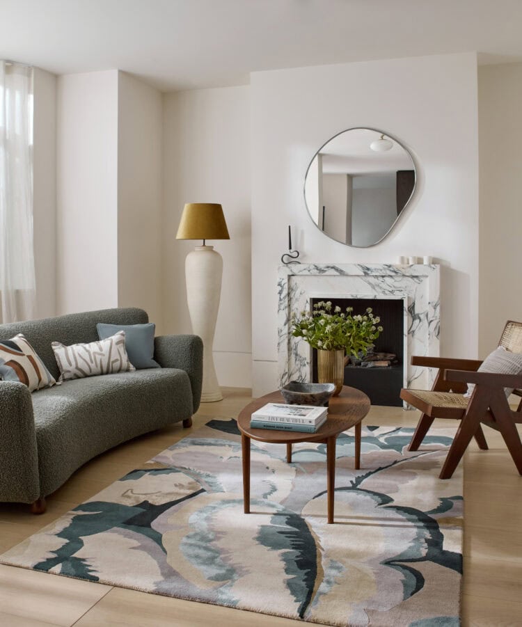 Stylish living room with grey sofa, marble fireplace, and round mirror.