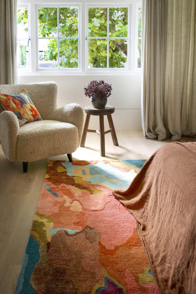 Cozy living room with armchair, colourful rug, and large window view of greenery.