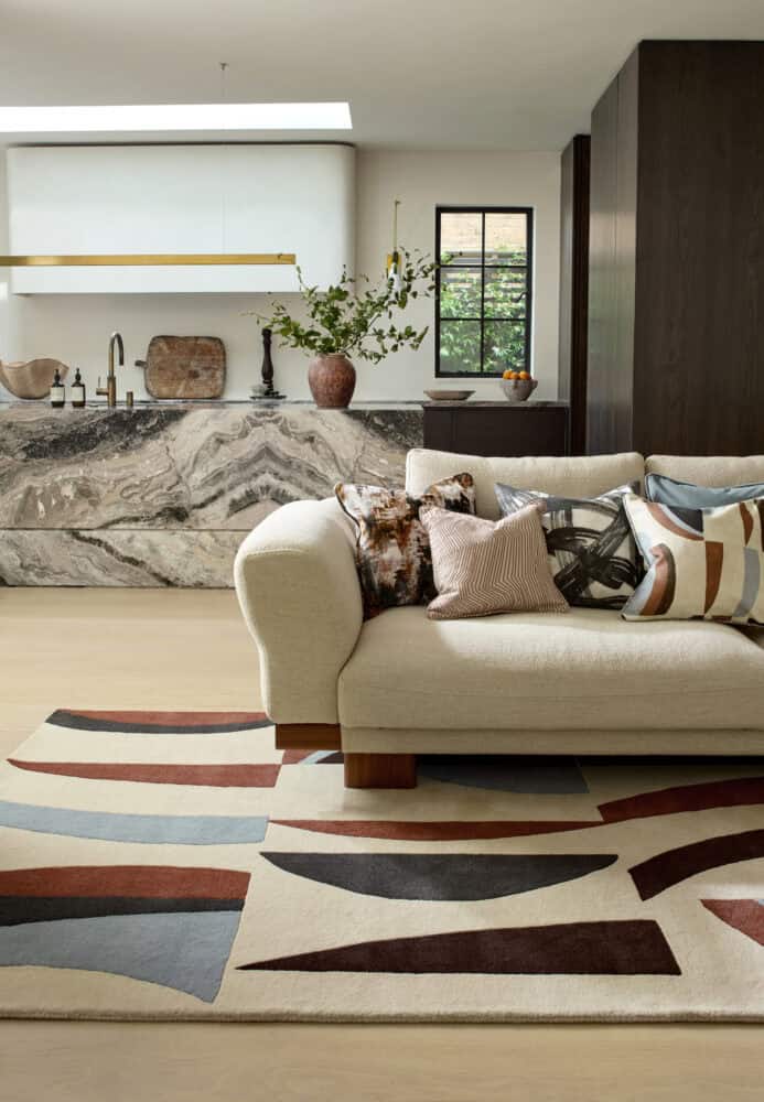 Stylish living room with cream sofa, patterned rug, and marble kitchen island.