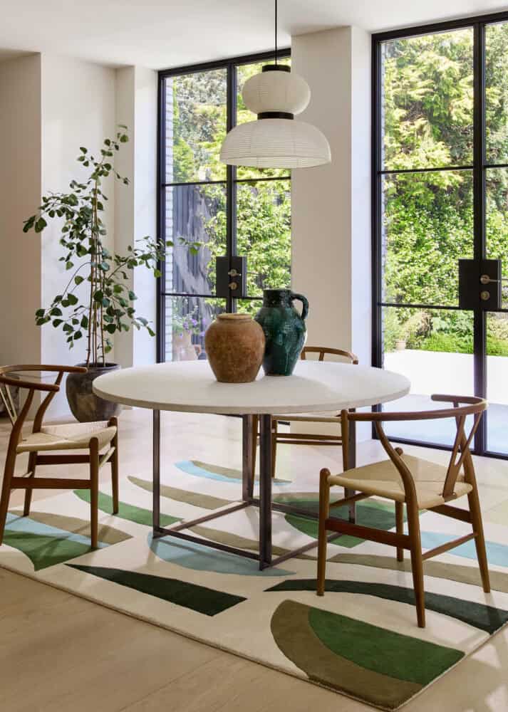 Bright dining room with large windows, round table, and wooden chairs.