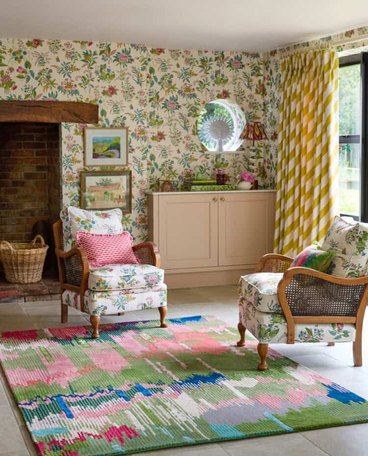 Charming living room with floral wallpaper, vintage armchairs, and colourful rug.